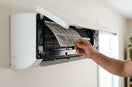 Close-up of a wall-mounted Mitsubishi mini split indoor unit with the front panel open, showing a hand removing the white filter for replacement